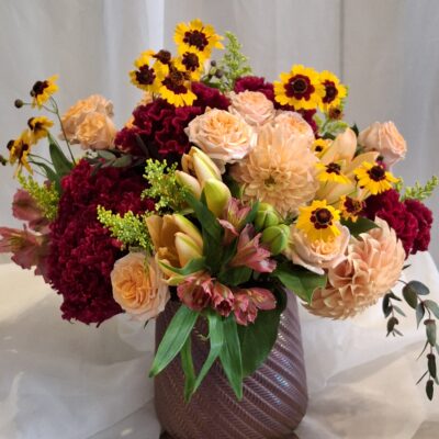 This Autumn mix combines peach dahlias, red cockscom, orange Peruvian lily, roses and fall color fillers.