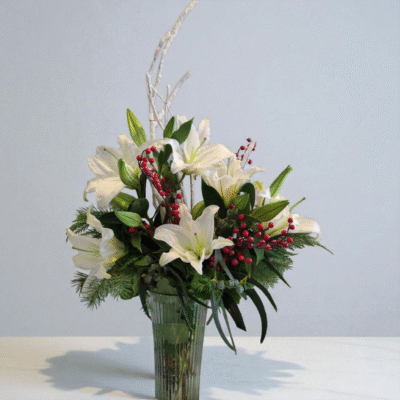 This Elegant arrangment of White Christmas lilies, snowy branches, red berries and Christmas greens would be a lovely treat this holiday season.