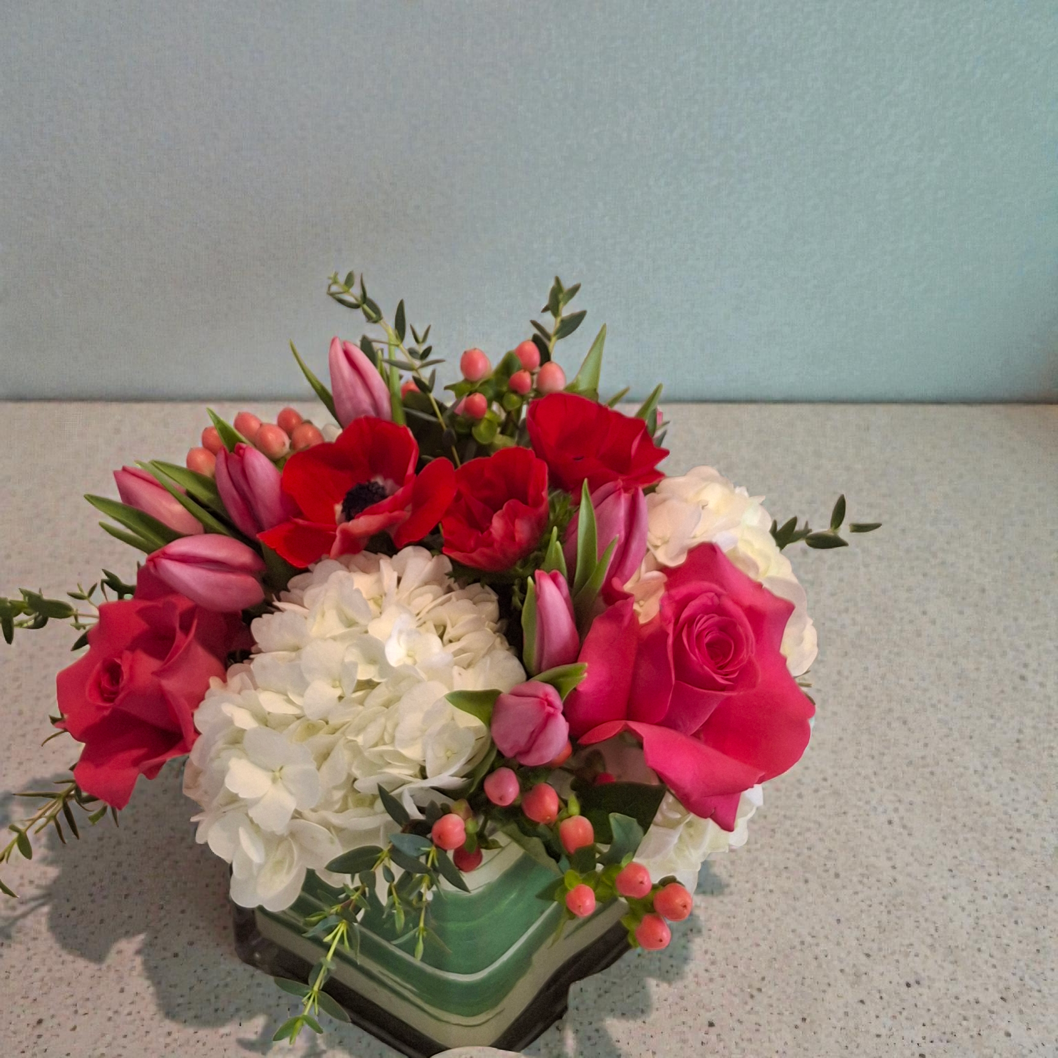 This beautiful arrangement is a display of pleasing colors filled with hydrangeas, tulips, anemones, pink coffee beans and Pink Floyd Roses all in a square vase.